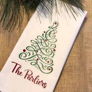K&ouml;nnte beinhalten: Wei&szlig;es K&uuml;chentuch mit einem gr&uuml;nen und roten Weihnachtsbaumdesign und dem Text "The Parliers" in Rot.