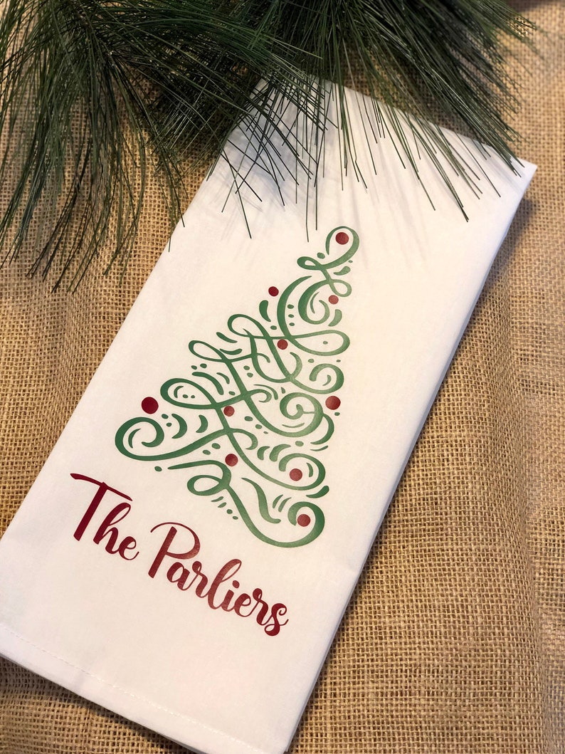K&ouml;nnte beinhalten: Wei&szlig;es K&uuml;chentuch mit einem gr&uuml;nen und roten Weihnachtsbaumdesign und dem Text "The Parliers" in Rot.