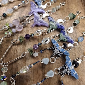 May include: A collection of hanging ornaments featuring moth-shaped charms in shades of blue, purple, and green. Each piece is constructed with silver-toned metal chains, assorted gemstone beads, small white crescent moon charms, and star-shaped accents.