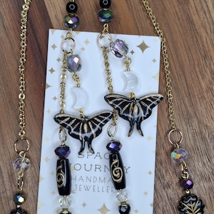 May include: Gold-toned eyeglass chains with black and gold moth pendants, black and iridescent beads, and clear crystal accents. The chains are attached to a white card with the text "SPACE JOURNEY HANDMADE JEWELLER".