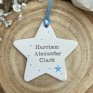May include: White ceramic star ornament with blue polka dots and a blue star. The ornament has the names "Harrison Alexander Clark" written on it.