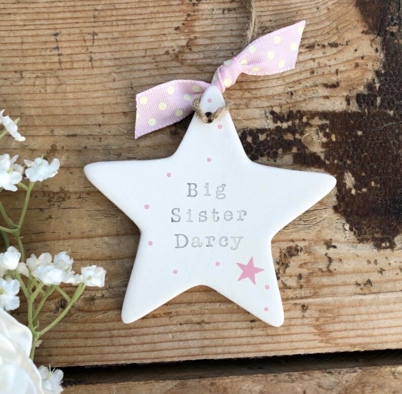 May include: White ceramic star ornament with pink polka dots and the text "Big Sister Darcy".