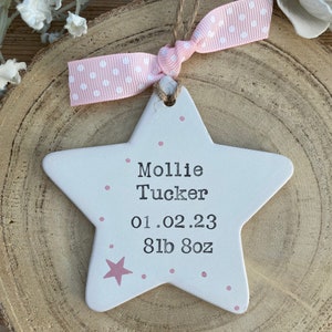 May include: White ceramic star ornament with pink polka dots and a pink star. It says "Mollie Tucker 01.02.23 8lb 8oz" in black lettering.