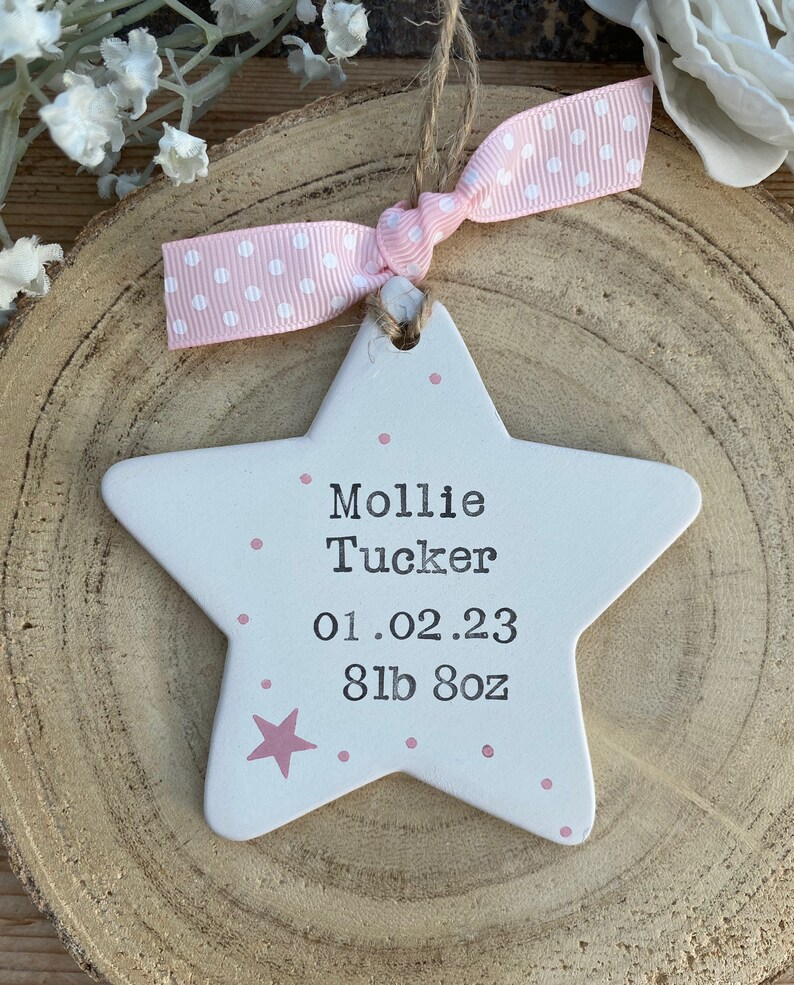 May include: White ceramic star ornament with pink polka dots and a pink star. It says "Mollie Tucker 01.02.23 8lb 8oz" in black lettering.