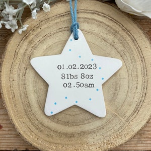 May include: White ceramic star ornament with blue dots and the text "01.02.2023 8 lbs 8oz 02.50am" on it.
