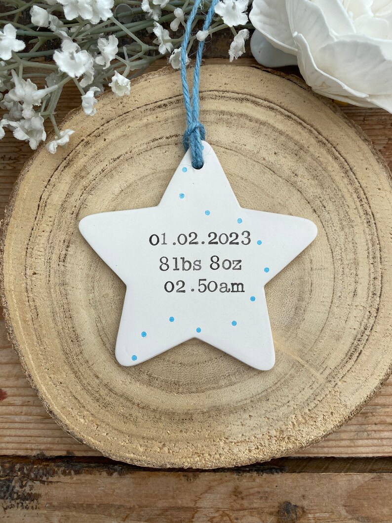 May include: White ceramic star ornament with blue dots and the text "01.02.2023 8 lbs 8oz 02.50am" on it.