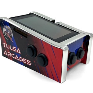 May include: A red, blue, and black arcade cabinet with a silver trim. The cabinet has a screen, three buttons, and the text "TULSA ARCADES" on the side.