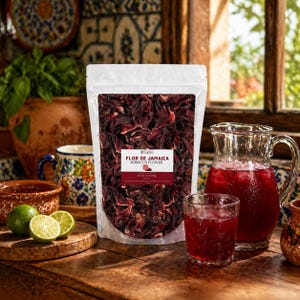 May include: A bag of dried hibiscus flowers, labelled "Flor de Jamaica Hibiscus Flower", sits on a wooden table. A jug and a glass of red hibiscus tea are next to the bag. Limes and a mug are also on the table.
