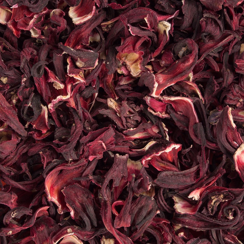 May include: A close-up shot of dried hibiscus flowers, displaying deep red petals with pale edges. The petals are curled and layered, creating a textured appearance. The image highlights the natural, organic form of the dried flowers, often used for herbal teas.