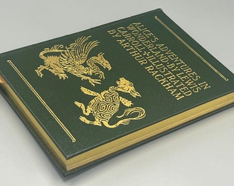 Puede incluir: Un libro de tapa dura verde con letras doradas e ilustraciones. El título es "Alice's Adventures in Wonderland" de Lewis Carroll, ilustrado por Arthur Rackham.