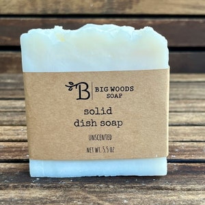 May include: A white bar of unscented solid dish soap with a brown paper label that reads "Big Woods Soap" and "solid dish soap unscented net wt. 5.5 oz."