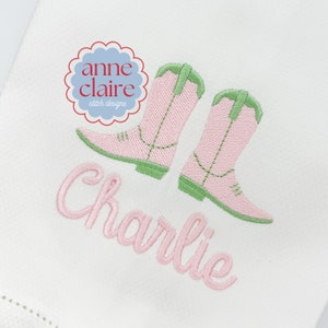 May include: Pink embroidered cowboy boots with green trim and the name "Charlie" embroidered in pink below.