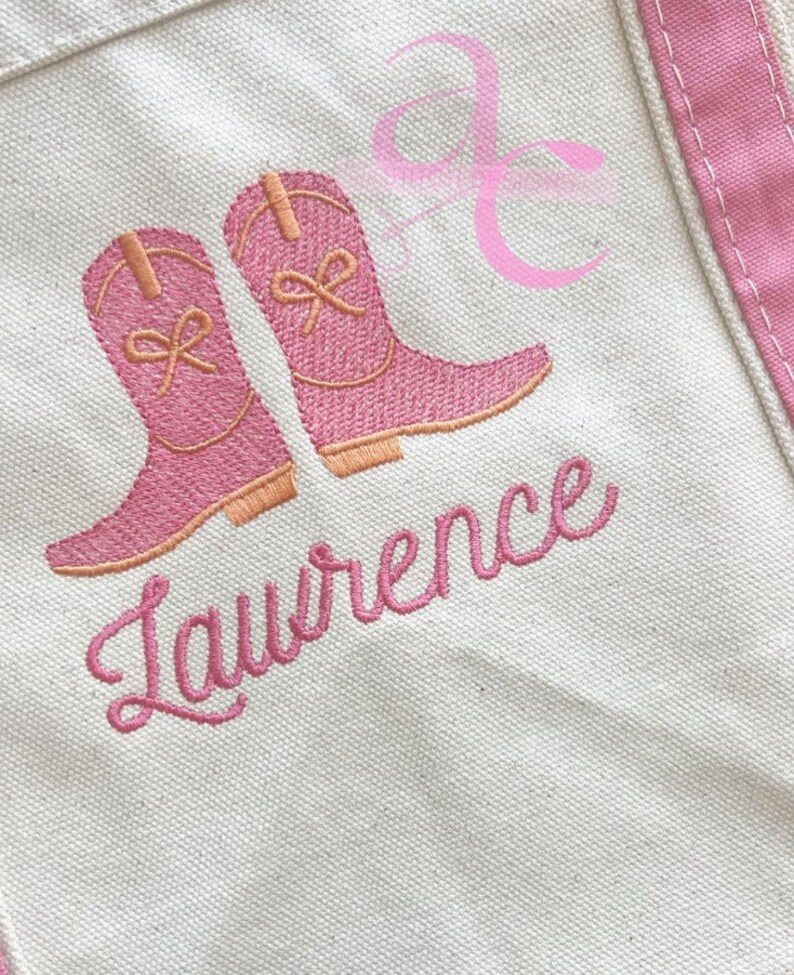 Peut inclure: Un sac fourre-tout en toile avec des bordures roses et des bottes de cowboy roses brod&eacute;es. Le nom "Lawrence" est brod&eacute; en script rose en dessous. Un motif de ruban rose est dans le coin sup&eacute;rieur droit.