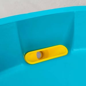 Könnte beinhalten: Nahaufnahme eines blauen Plastik-Kinderbeckens mit einem gelben Ablassstopfen.