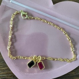 May include: A gold chain bracelet with two charms, one black and one red.