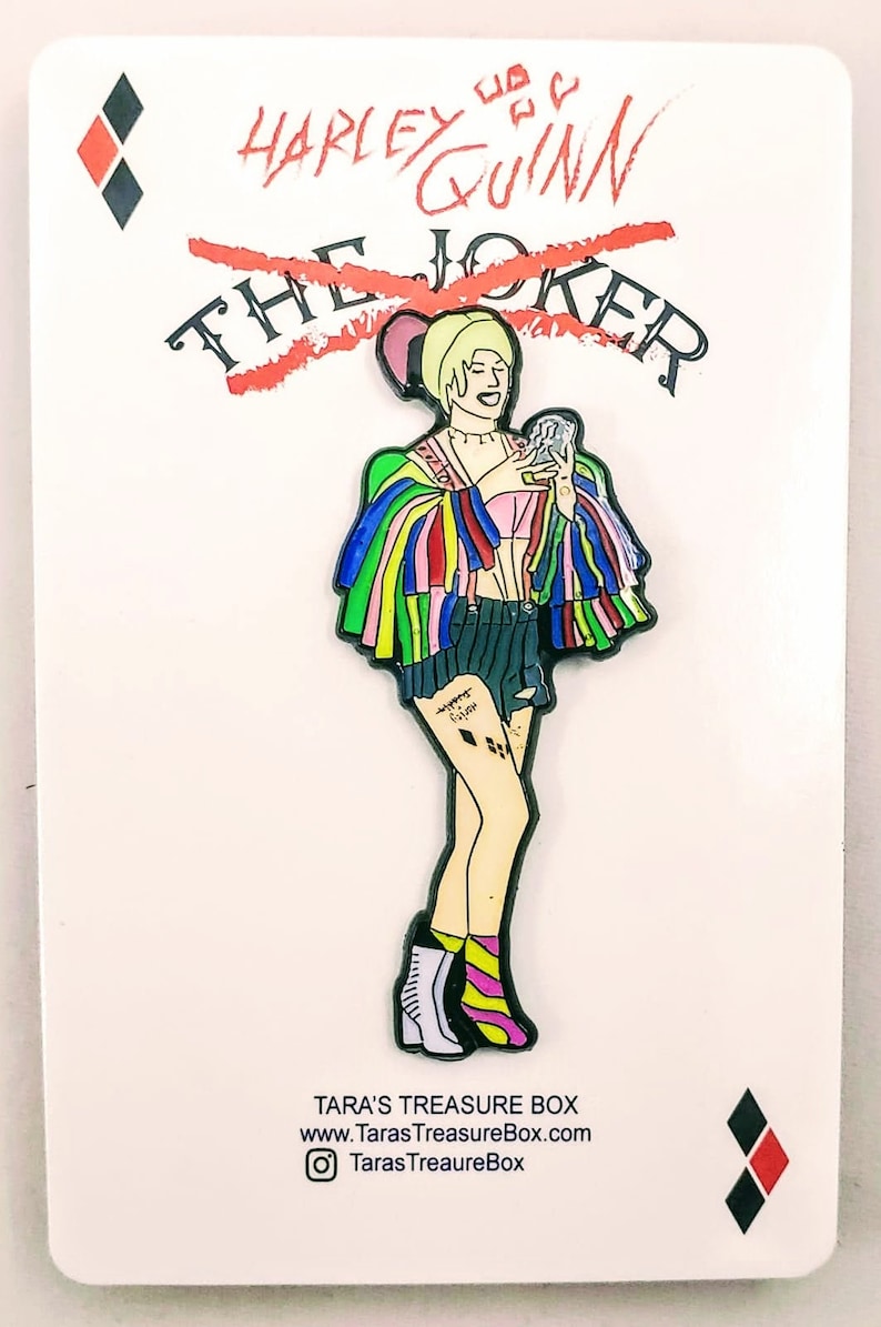 May include: Harley Quinn enamel pin with a red line through the word "The" and the word "Joker". Harley is wearing a colorful jacket, pink top, denim shorts, and black boots. The pin is on a white background with a diamond card suit in the corner.
