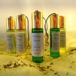 May include: Five small glass bottles with gold lids and black strings. Each bottle contains a clear liquid and has a white label with the text "Energy Boost" and "Miscela di olio by Nicole".
