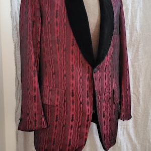 May include: A red and black patterned blazer with a black velvet collar. The blazer has a single-button closure and two front pockets. The fabric has a vertical stripe design.