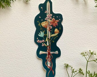 May include: A sticker featuring a sword with a bouquet of flowers tied around the hilt with a red ribbon. The flowers are pink, yellow, and blue. The background is a dark teal color.