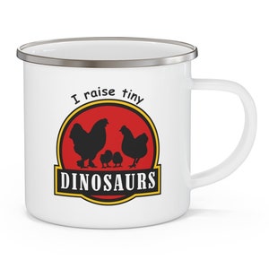 May include: White enamel mug with a black and yellow graphic that reads "I raise tiny DINOSAURS". The graphic features silhouettes of chickens and chicks inside a red circle. The mug has a silver rim and a white handle.