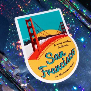 Sticker with a teal sky and yellow sun with the red Golden Gate Bridge. In teal script lettering it reads, San Francisco, and around it reads, In sunny northern California... in the summertime! Sticker rests on a holographic blue background.
