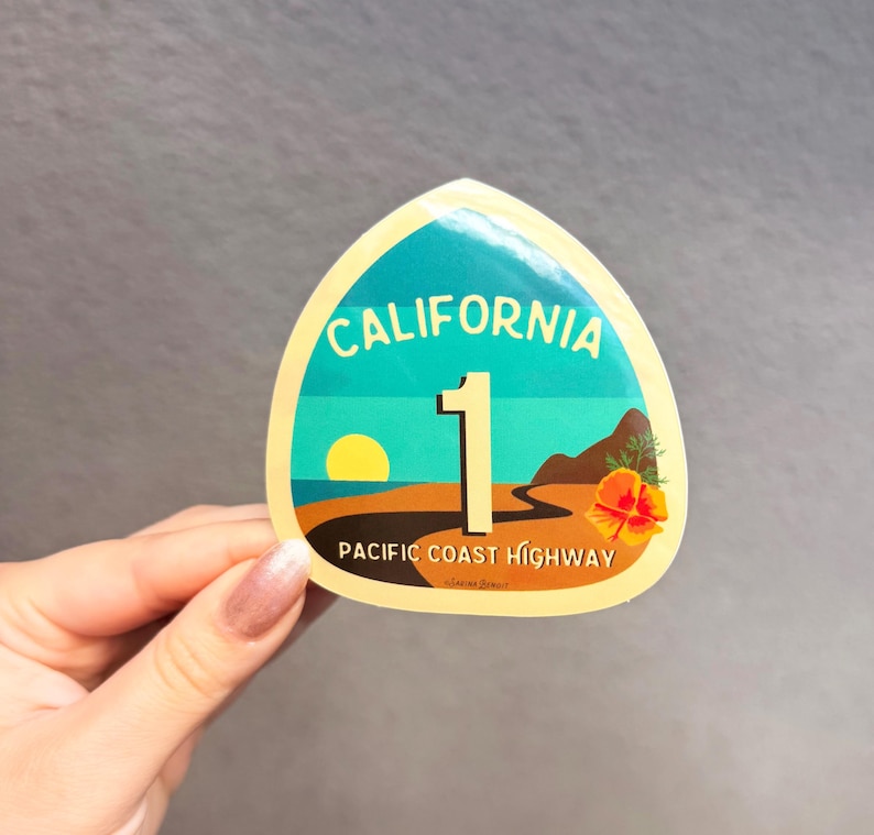May include: A yellow and blue California Highway 1 sticker with a sunset and a poppy flower. The sticker says "California 1 Pacific Coast Highway".