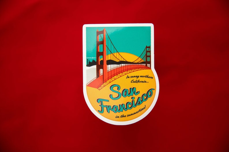 Sticker with a teal sky and yellow sun with the red Golden Gate Bridge. In teal script lettering it reads, San Francisco, and around it reads, In sunny northern California... in the summertime! Sticker rests on a red background.