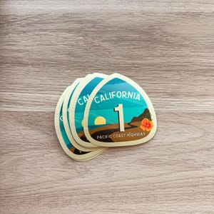May include: A stack of five yellow and blue California Highway 1 stickers with the text "PACIFIC COAST HIGHWAY" on the bottom.