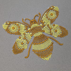May include: Embroidered bee design in yellow and brown on a gray background. The bee has detailed wings and body, with a stylized, geometric pattern. The embroidery is likely for a patch or applique.