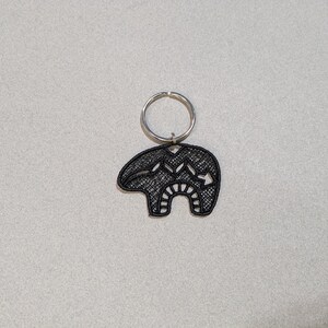 May include: Black metal keychain featuring a stylized bear design with intricate details. The bear is attached to a silver key ring.