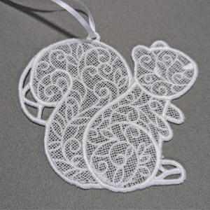 May include: White, intricately embroidered squirrel ornament with a delicate, openwork design. The squirrel has a fluffy tail and is suspended by a white ribbon. The ornament is approximately 4 inches tall.