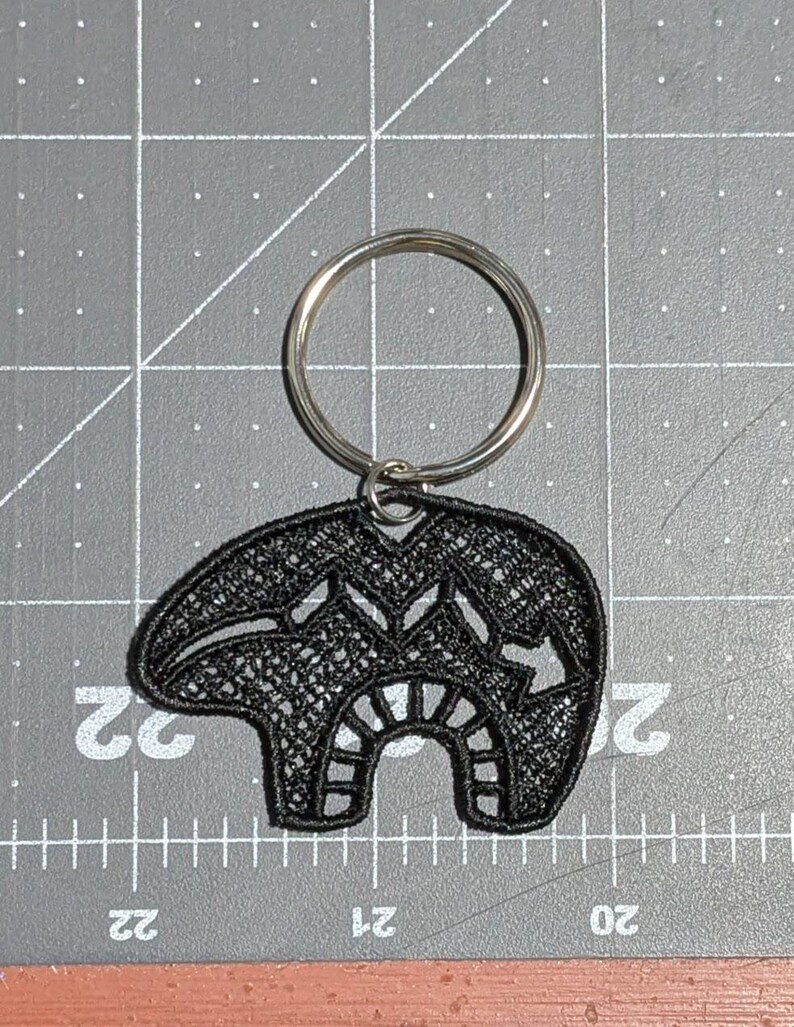 May include: Black embroidered bear keychain with a silver key ring. The bear is a traditional design with intricate details.