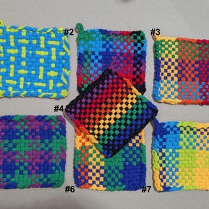 May include: A collection of seven woven potholders in various colors. Each potholder is square-shaped with a loop for hanging. Colors include blue, yellow, green, red, purple, and rainbow patterns. The potholders are handmade and have a textured appearance.