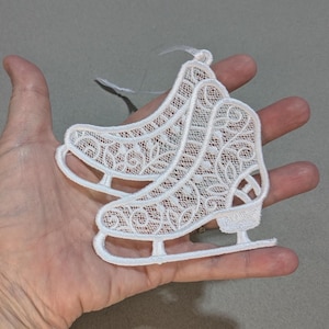 May include: White lace ice skate ornaments. These decorative ornaments feature intricate lace detailing and are designed in the shape of ice skates. Each ornament has a white ribbon for hanging. Perfect for winter holiday decor.