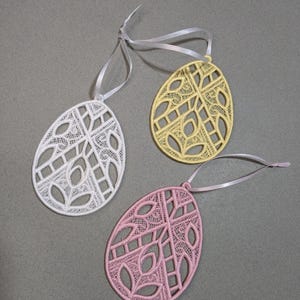 May include: Three decorative Easter eggs made of white, yellow, and pink lace. Each egg has a delicate, intricate design and a ribbon for hanging.