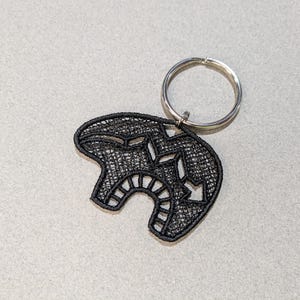 May include: Black embroidered key chain with a geometric design. The key chain is attached to a silver key ring.