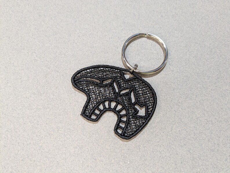 May include: Black embroidered key chain with a geometric design. The key chain is attached to a silver key ring.