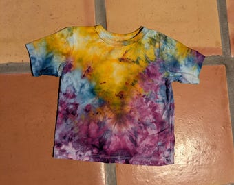 Camiseta infantil teñida a mano con la técnica Ice Dye, color amarillo y morado radiante con efecto tie-dye, talla 12-18 meses.
