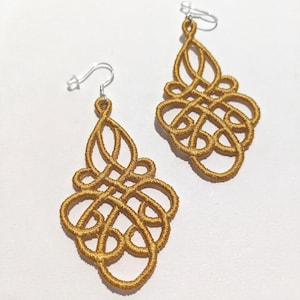 May include: A pair of gold-colored, intricately designed earrings. Each earring features a complex, knotted pattern suspended from a silver-colored ear wire. The earrings have a teardrop shape, with a detailed, openwork design.