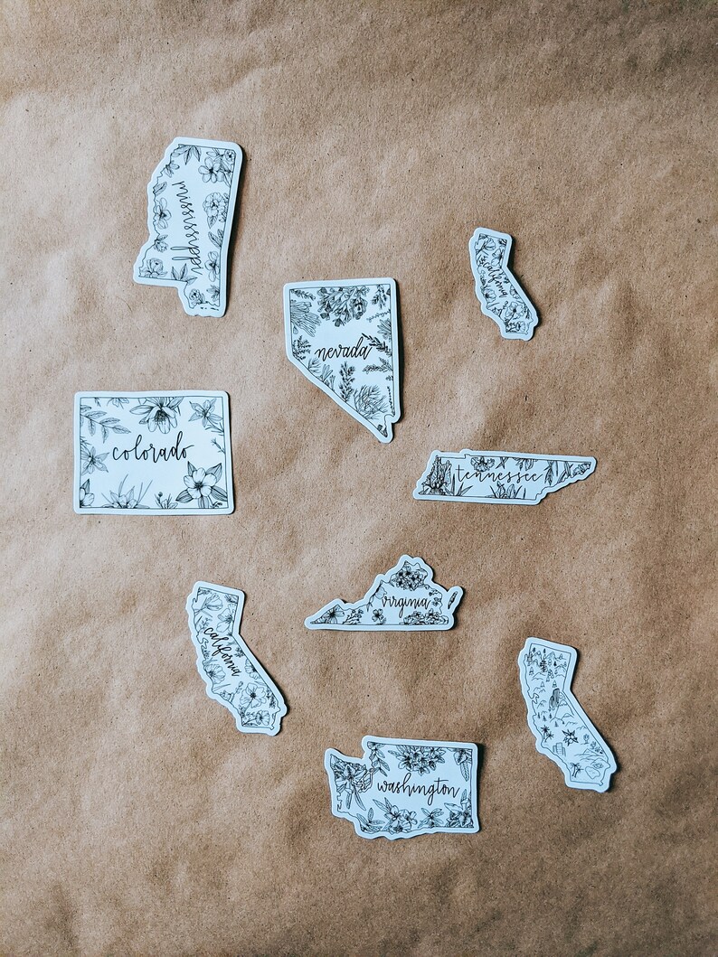 May include: A collection of white stickers featuring state outlines, each filled with floral illustrations and state names in a handwritten font. States include Mississippi, Nevada, Colorado, California, Tennessee, Virginia, and Washington.