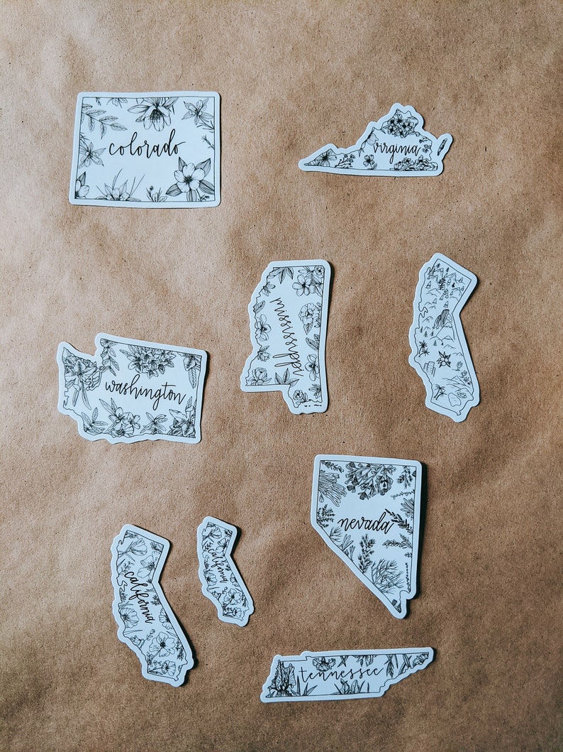 May include: A collection of white stickers featuring state outlines, each adorned with floral illustrations and state names in a handwritten font. States include Colorado, Virginia, Washington, Mississippi, California, Nevada, and Tennessee.