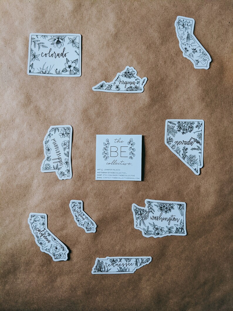 May include: A collection of white stickers featuring state outlines with floral illustrations and state names in cursive. States include Colorado, Virginia, Mississippi, Nevada, California, Tennessee, and Washington. A small card with the text "the BE collective" is also present.