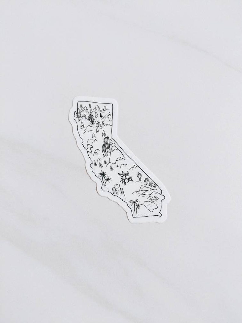 May include: A black and white sticker in the shape of California. The sticker features a detailed outline of the state with illustrations of mountains, trees, a desert landscape, and buildings. The sticker is on a white background.