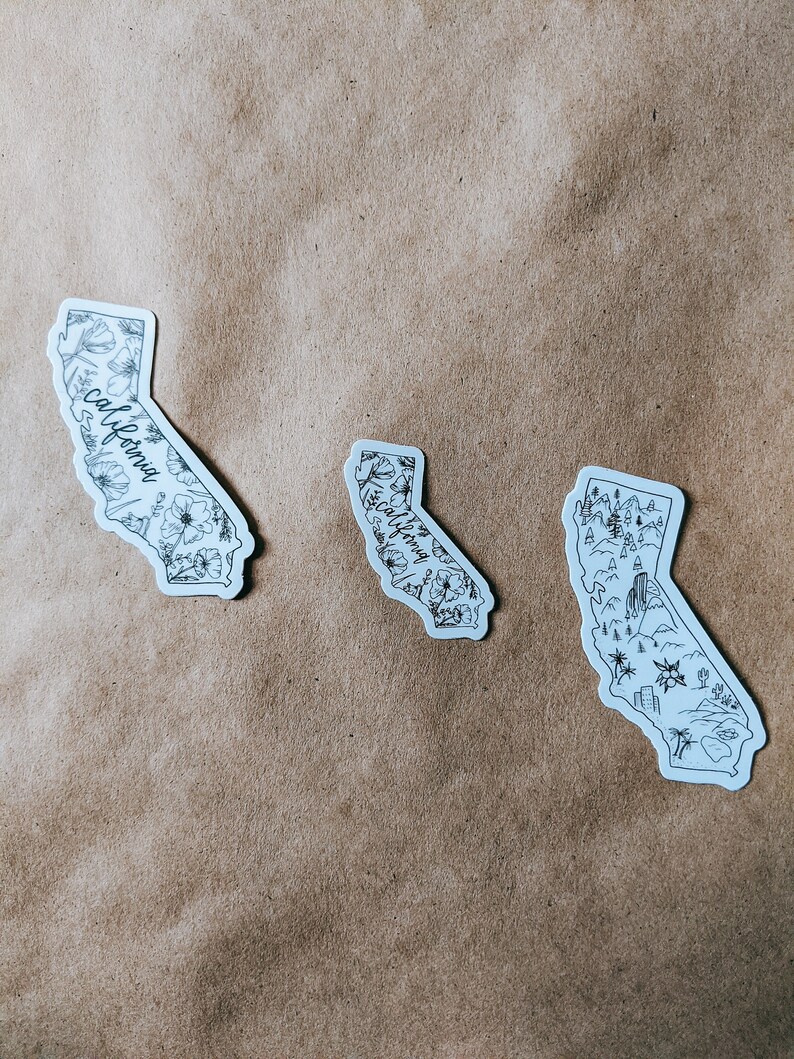 May include: Three white stickers in the shape of California. Each sticker features a black outline of the state with different designs: floral, botanical, and landscape illustrations. The word "California" is written on two of the stickers.