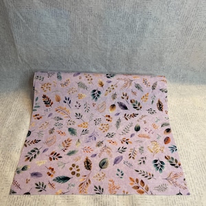 May include: A rectangular sheet of light purple fabric featuring a repeating pattern of small, multicolored leaves and sprigs in shades of orange, brown, green, and dark purple, arranged in a scattered, non-directional layout across the surface.