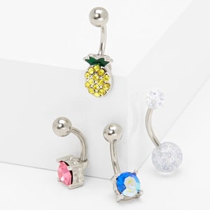 Könnte beinhalten: Set aus vier Bauchnabelringen mit verschiedenen Anhängern. Ein Ring hat einen glitzernden Ananas-Anhänger, ein anderer einen blauen Kristall-Anhänger, ein weiterer einen rosa Kristall-Anhänger und der letzte einen silbernen Glitzerball-Anhänger.