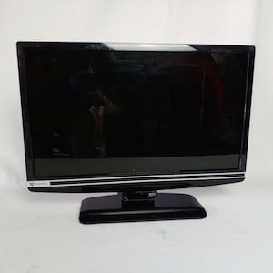 May include: A black Gateway flat-screen television with a rectangular screen and a black base. The screen is glossy and reflects the surrounding environment. The TV has a thin, silver accent line along the bottom edge.