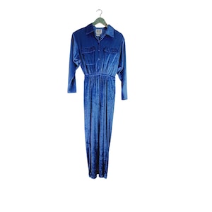 May include: A blue velvet jumpsuit with a collared button-up top and long sleeves. The jumpsuit has a fitted bodice and wide legs.