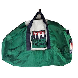 May include: Green and white duffel bag with a navy blue trim. The bag has a large white patch with the text "TH 44/840 SAILING GEAR" in red, blue, and white lettering.