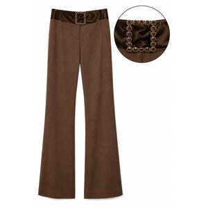 May include: Brown trousers featuring a wide, satin-finish waistband and a square-shaped buckle adorned with circular brown crystals. The trousers have a straight-leg cut with a subtle texture, and the buckle detail is highlighted in a circular inset.